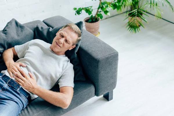 Homem bonito em t-shirt com dor de estômago deitado no sofá — Fotografia de Stock