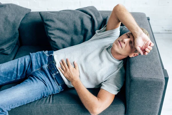 Homem bonito em t-shirt com dor de estômago deitado no sofá — Fotografia de Stock