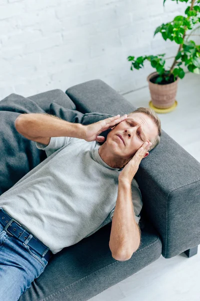 Visão de alto ângulo de homem bonito em t-shirt com olhos fechados tocando cabeça no apartamento — Fotografia de Stock
