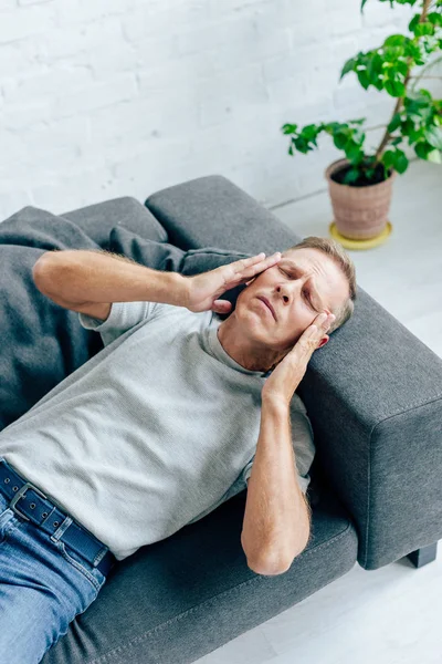 Vista de ángulo alto del hombre guapo en camiseta con los ojos cerrados tocando la cabeza en el apartamento - foto de stock