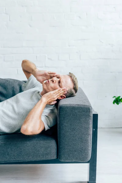 Homem bonito em t-shirt com olhos fechados tocando cabeça no apartamento — Fotografia de Stock