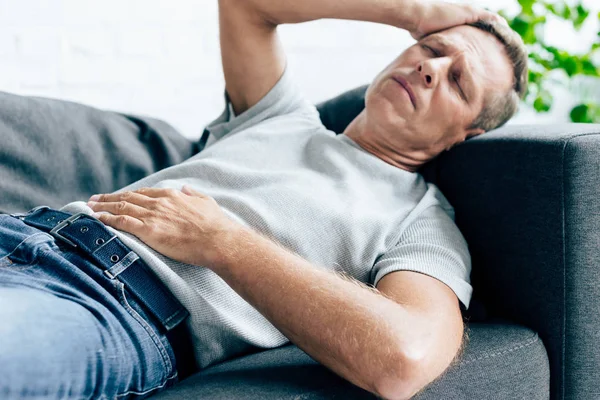 Hombre guapo en camiseta con los ojos cerrados tocando la cabeza en el apartamento - foto de stock