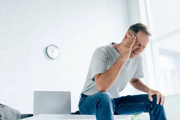 Handsome man in t-shirt with closed eyes touching head in apartment — Stock Photo