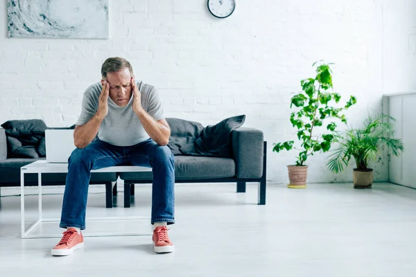 Bel homme en t-shirt avec les yeux fermés touchant la tête dans l'appartement — Photo de stock