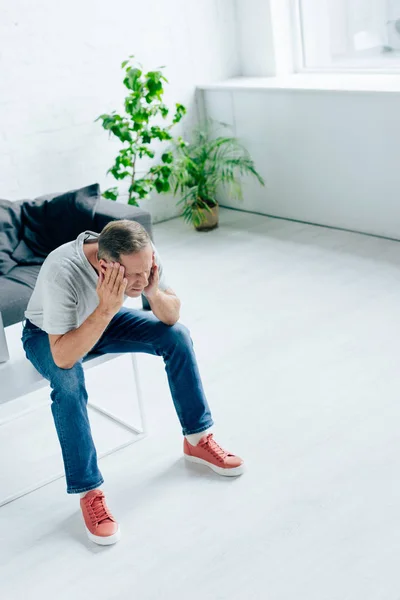 Vue grand angle du bel homme en t-shirt touchant la tête dans l'appartement — Photo de stock