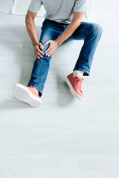 Vista ritagliata dell'uomo in t-shirt sensazione di dolore al ginocchio in appartamento — Foto stock