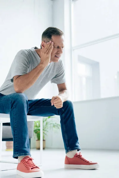 Bel homme en t-shirt avec les yeux fermés touchant la tête dans l'appartement — Photo de stock
