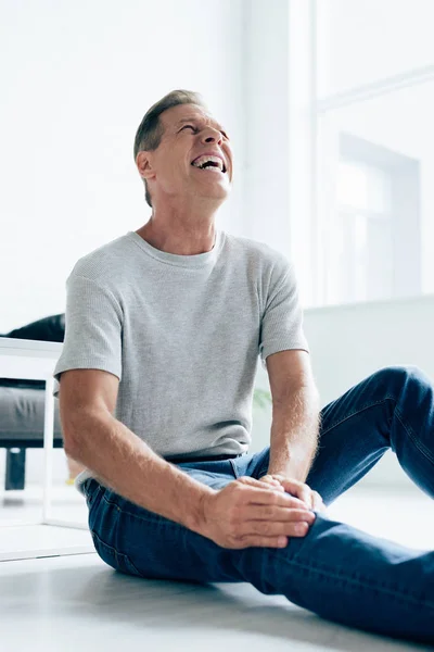 Handsome man in t-shirt feeling pain in knee in apartment — Stock Photo