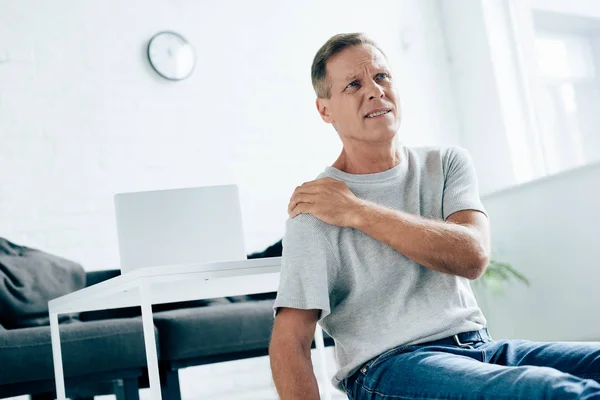 Bello uomo in t-shirt sensazione di dolore alla spalla in appartamento — Foto stock