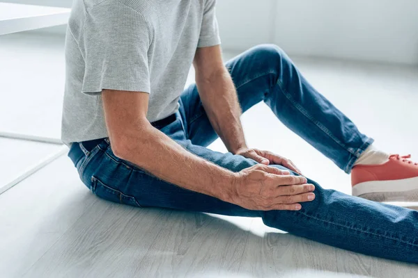 Vista ritagliata dell'uomo in t-shirt sensazione di dolore al ginocchio in appartamento — Foto stock