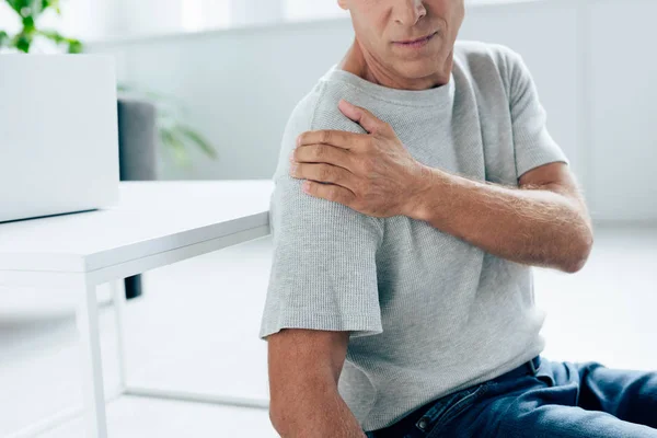 Обрізаний вид чоловіка в футболці відчуває біль в плечі в квартирі — стокове фото