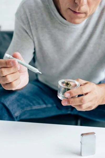 Cropped view of man in t-shirt holding blunt and medical marijuana buds — Stock Photo