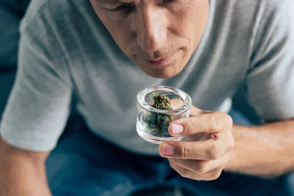 Cropped view of man in t-shirt smelling medical cannabis in apartment — Stock Photo