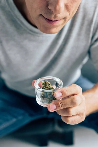 Vista recortada del hombre en camiseta mirando cannabis medicinal en apartamento - foto de stock