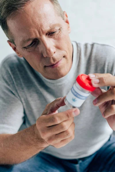 Homem bonito em t-shirt olhando para cannabis medicinal no apartamento — Fotografia de Stock