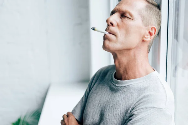 Homem bonito fumando embotado com cannabis medicinal no apartamento — Fotografia de Stock