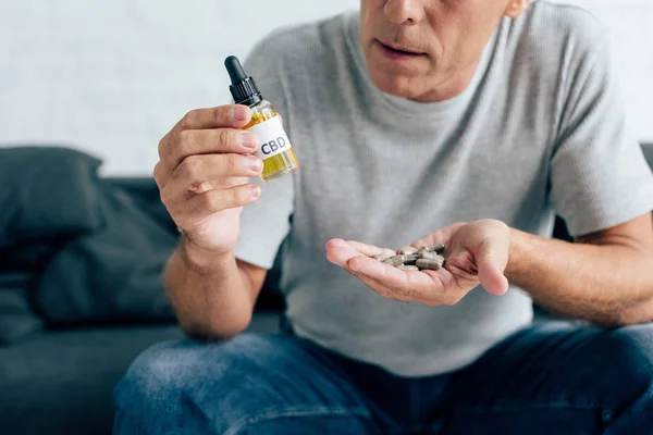 Vista recortada del hombre en camiseta sosteniendo píldoras y aceite de cannabis - foto de stock