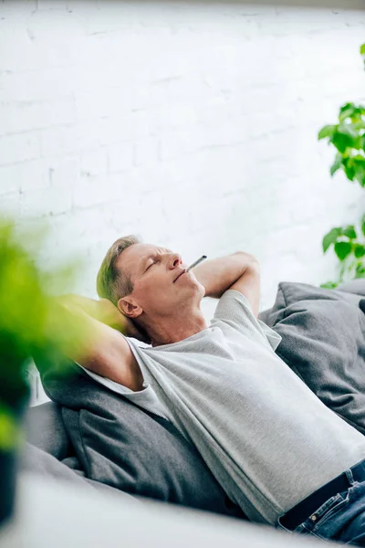 Selective focus of handsome man smoking blunt with medical cannabis in apartment — Stock Photo