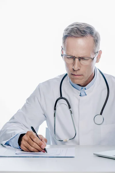 Handsome doctor in white coat writing with pen isolated on white — Stock Photo