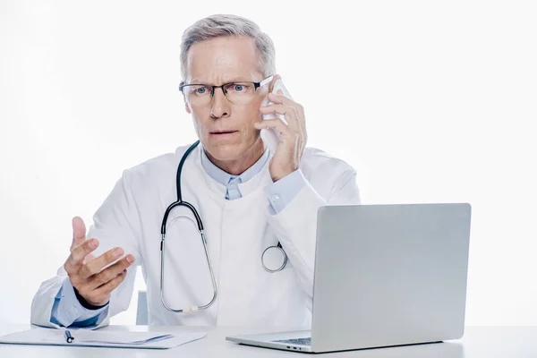 Schöner Arzt in weißem Mantel, der auf dem Smartphone isoliert auf weißem Grund spricht — Stockfoto