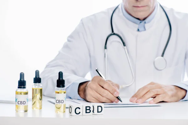 Обрезанный вид врача в белом халате письма с ручкой изолированы на белом — стоковое фото