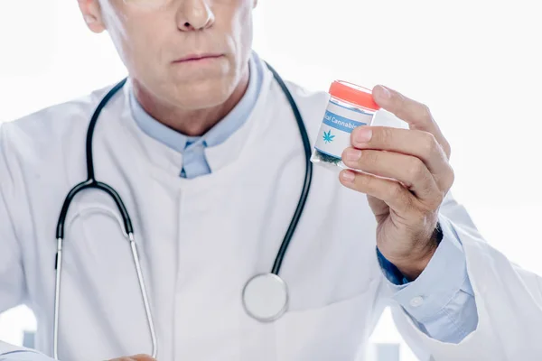 Vista recortada del médico de bata blanca que sostiene cannabis medicinal aislado sobre blanco - foto de stock