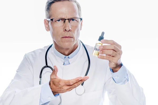 Guapo doctor en bata blanca sosteniendo aceite de cannabis aislado en blanco - foto de stock