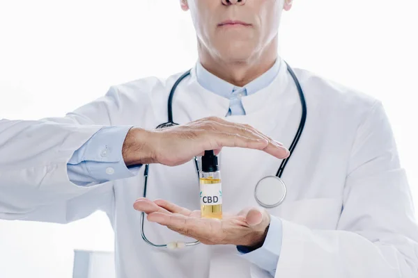 Vista recortada del médico de bata blanca sosteniendo aceite de cannabis aislado en blanco - foto de stock