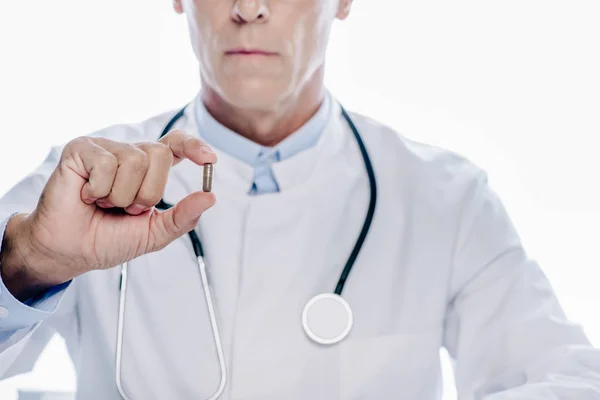 Vista recortada del médico de bata blanca sosteniendo píldora aislada en blanco — Stock Photo