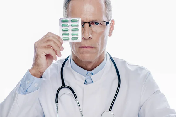 Médico bonito no casaco branco segurando pílulas isoladas no branco — Fotografia de Stock