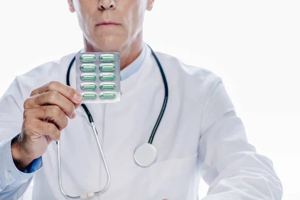 Обрезанный вид врача в белом халате с таблетками, изолированными на белом — стоковое фото