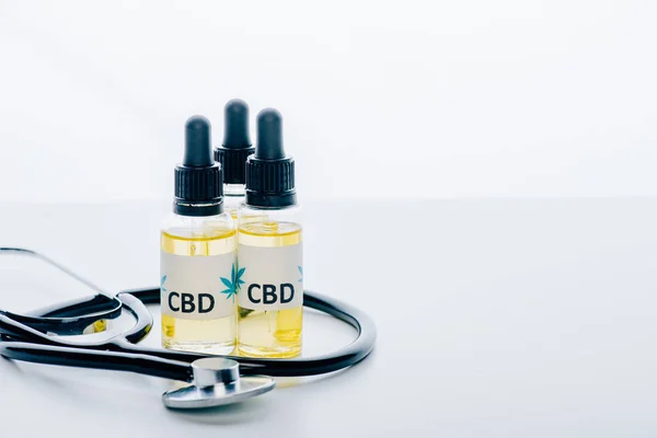 Cannabisöl in Flaschen mit Schriftzug cbd und Stethoskop auf weißem Hintergrund — Stockfoto