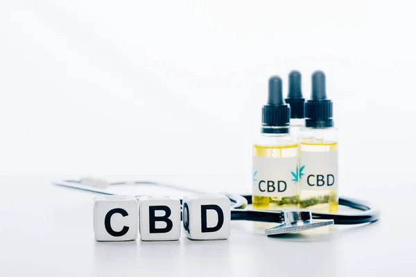 Cannabis oil in bottles with lettering cbd, cubes and stethoscope on white background — Stock Photo