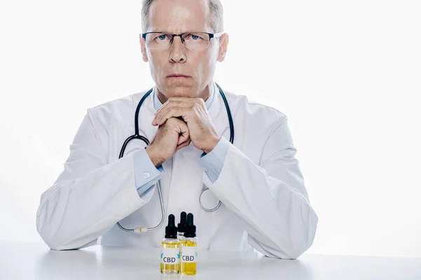 Handsome doctor in white coat with cbd on table isolated on white — Stock Photo