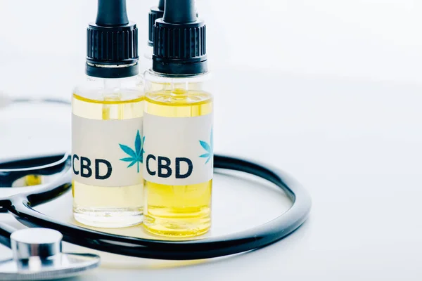 Óleo de cannabis em garrafas com letras cbd e estetoscópio sobre fundo branco — Fotografia de Stock