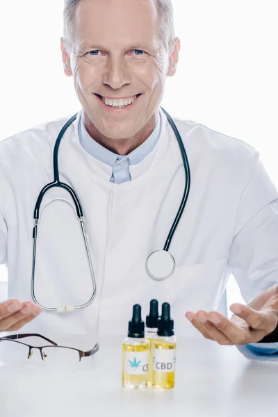 Handsome doctor in white coat with cbd on table isolated on white — Stock Photo