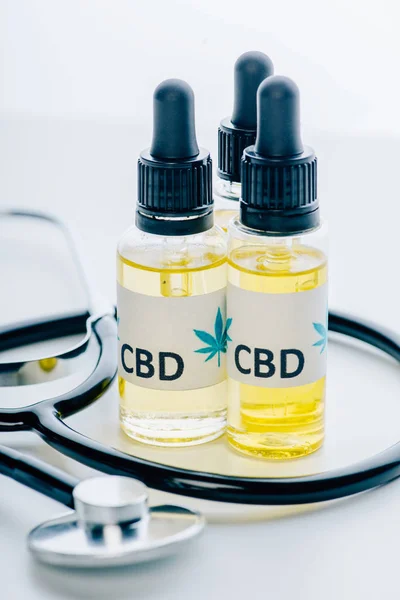 Масло каннабиса в бутылках с надписью cbd и стетоскоп на белом фоне — стоковое фото