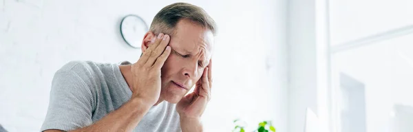 Plano panorámico del hombre guapo con dolor de cabeza en el apartamento - foto de stock