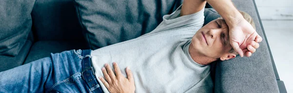 Panoramic shot of handsome man with stomachache in apartment — Stock Photo