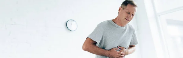 Panoramic shot of handsome man with stomachache in apartment — Stock Photo