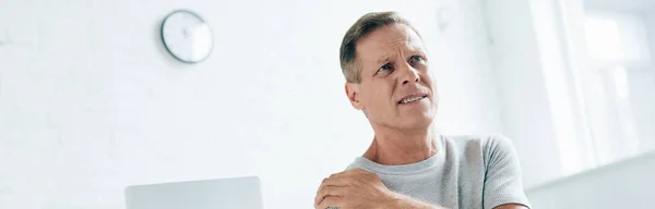 Panoramic shot of handsome man feeling pain in shoulder in apartment — Stock Photo