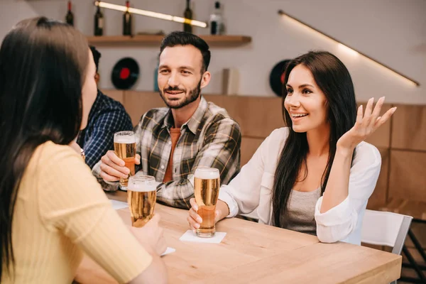 Amigos multiculturais alegres conversando enquanto bebem cerveja no pub — Fotografia de Stock