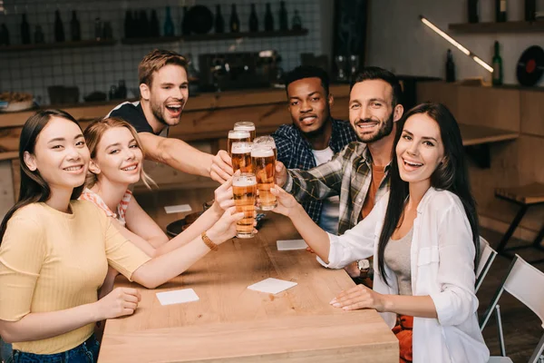 Amigos multiculturales sonriendo a la cámara mientras brindan con vasos de cerveza ligera - foto de stock