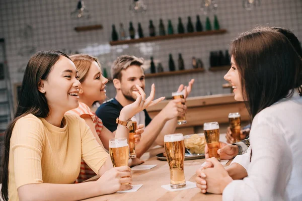 Весёлые мультикультурные друзья разговаривают за бокалом пива в пабе — стоковое фото
