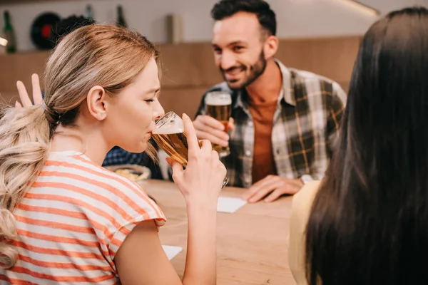 Mujer joven haciendo gestos mientras bebe cerveza ligera con los ojos cerrados - foto de stock