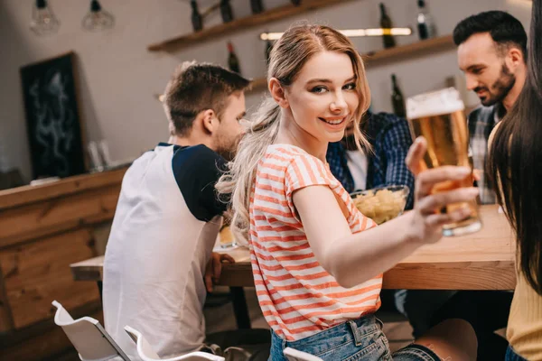 Foco seletivo de sorrir jovem mulher olhando para a câmera enquanto segurando vidro de cerveja leve — Fotografia de Stock