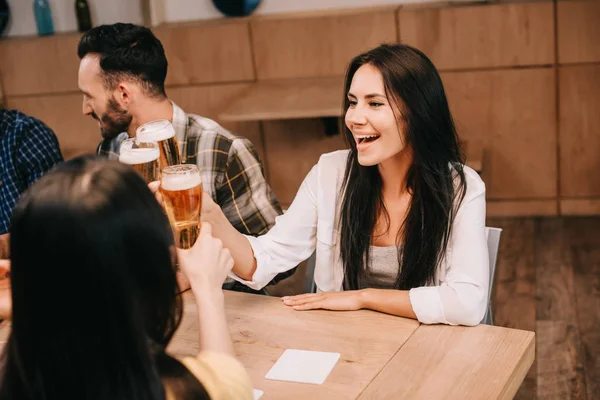 Attraente giovane donna clinking occhiali di birra leggera con gli amici — Foto stock