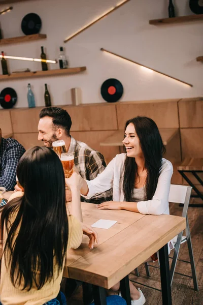 Jóvenes amigos tintineando vasos de cerveza ligera mientras pasan tiempo juntos en el pub - foto de stock