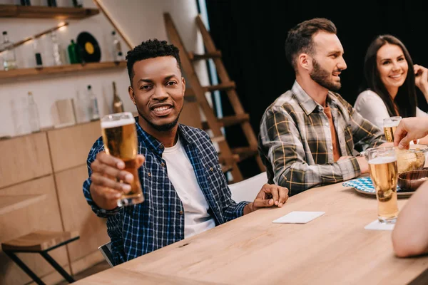 Lächelnder afrikanisch-amerikanischer Mann blickt in die Kamera, während er mit multikulturellen Freunden im Pub sitzt — Stockfoto