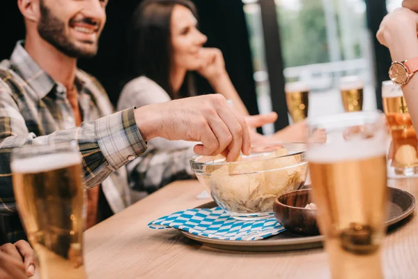 Partial view of man taking chips from bowl while sitting with friends in pub — Stock Photo